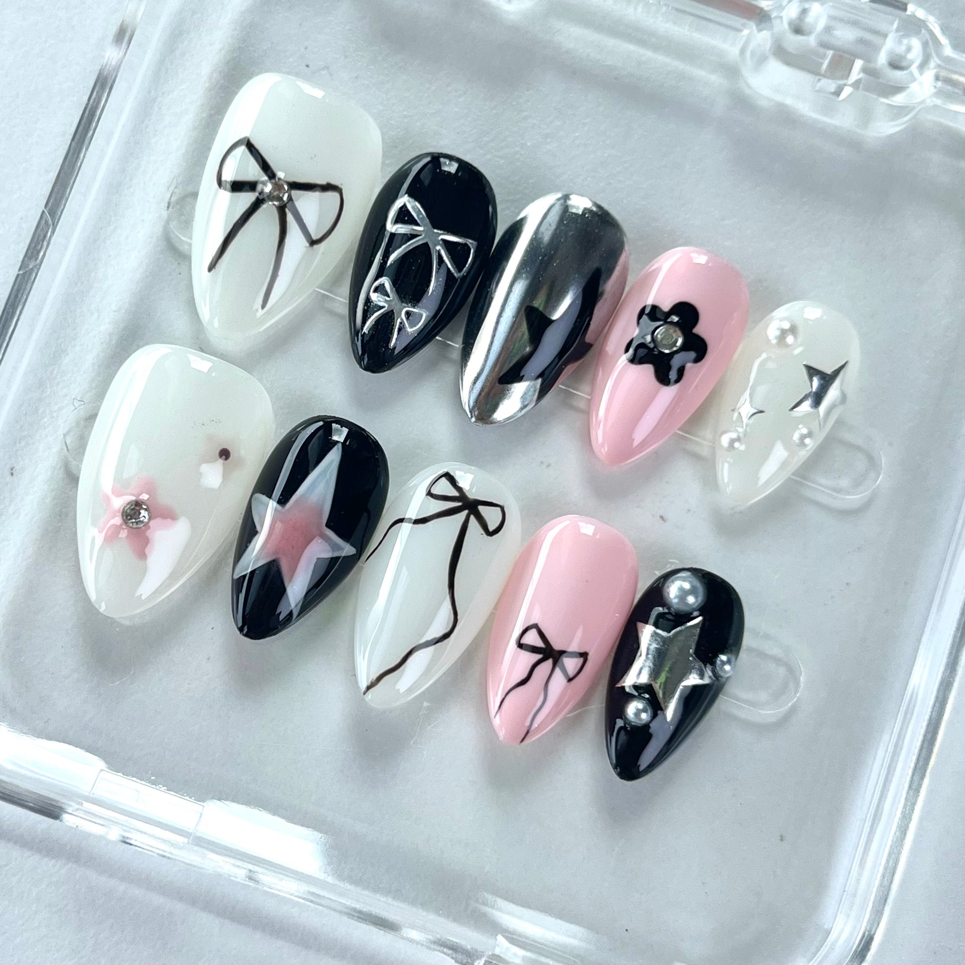 A set of press - on nails with a glamorous mix of pink and black colors, featuring stylish designs such as bows, stars, and flowers. The nails have a chic and fashionable appearance, suitable for both casual and formal events.