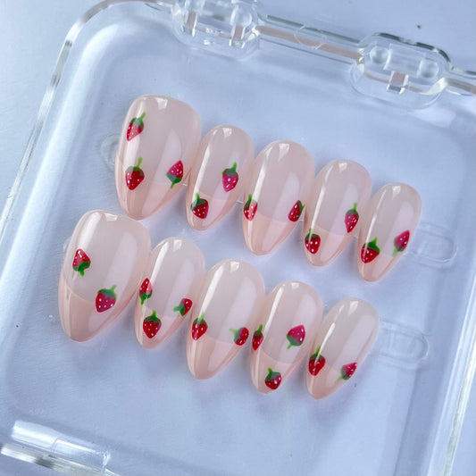 Pale pink nails adorned with hand-painted red strawberries and green leaves. This design captures the essence of a summer garden, blending fun and sophistication effortlessly.