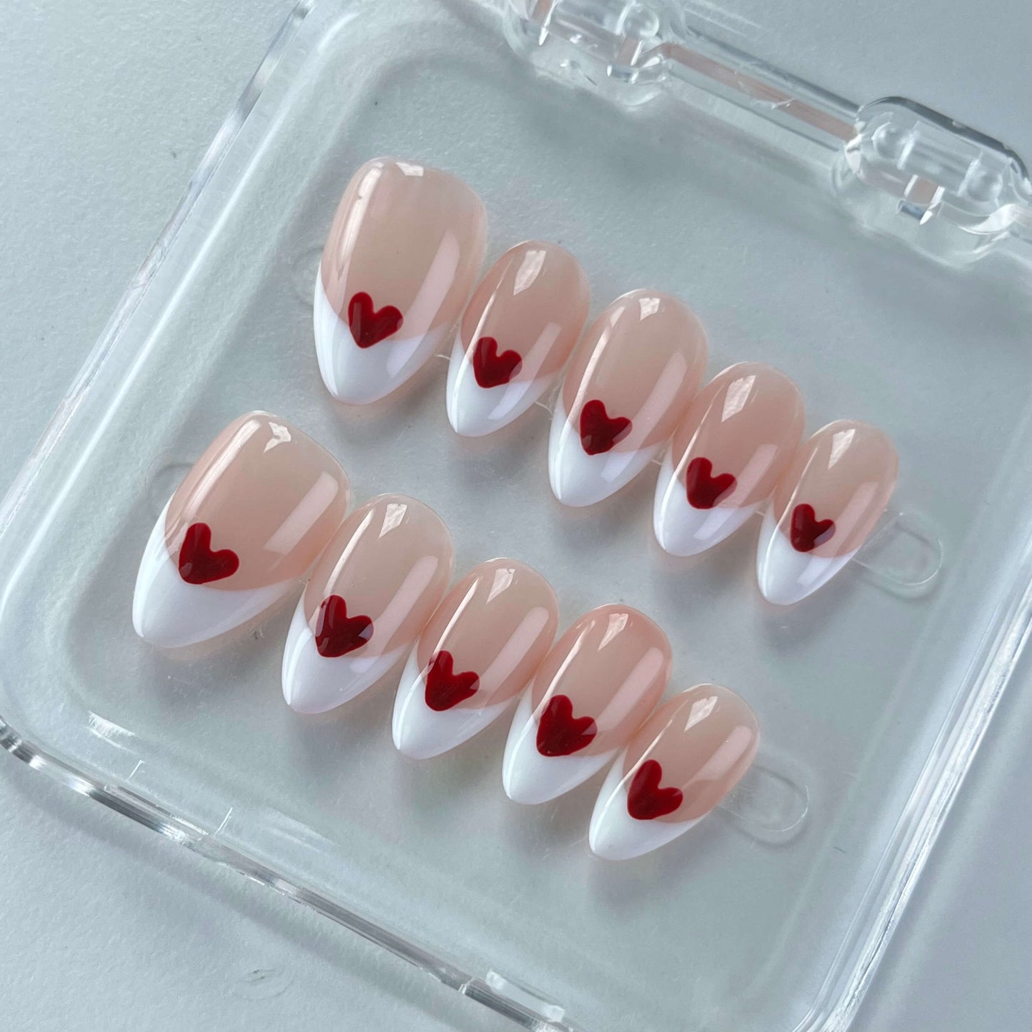 A romantic nail design named "Lovers’ Symphony," showcasing nude nails with soft red-to-white gradient French tips, each adorned with a perfectly placed red heart. This design evokes the tender harmony of love and connection, making it a perfect match for date nights or anniversaries.