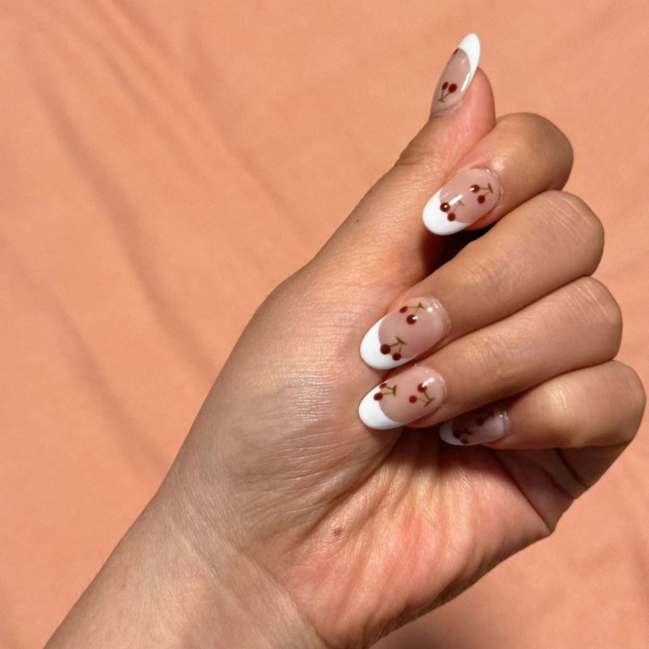 Nude nails with white French tips, beautifully decorated with dainty red cherries and green stems. This design captures the simplicity and elegance of a summer orchard, offering a graceful yet playful touch.