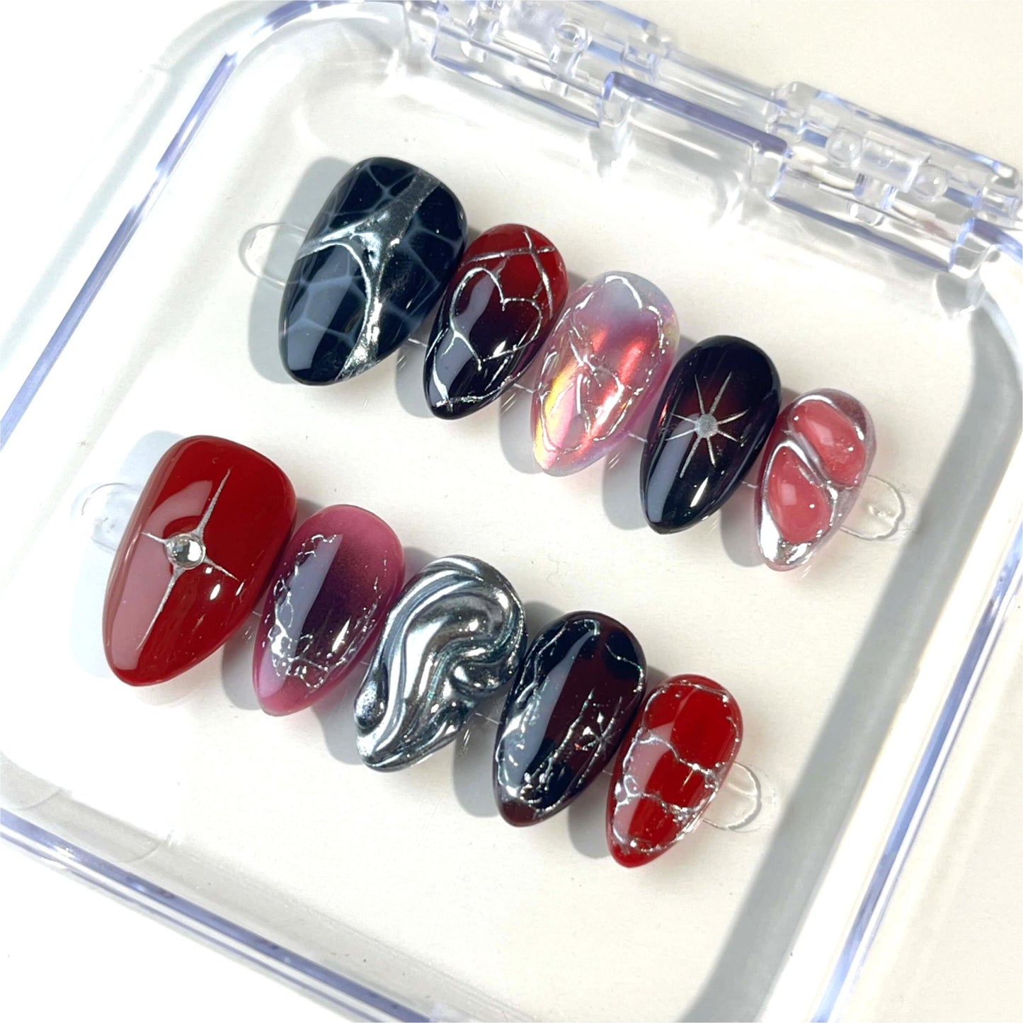 A set of handmade press-on nails featuring deep crimson and black tones, silver chrome details, radiant heart patterns, and a glossy finish. The perfect blend of passion and elegance for a bold, sophisticated look.