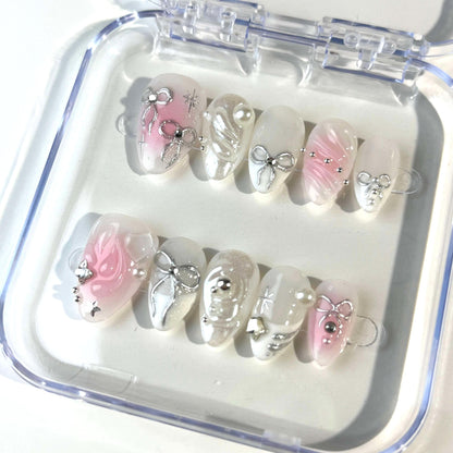 A set of press-on nails featuring pastel pink and white tones adorned with silver bows, pearls, and shimmering accents. The design exudes elegance and sophistication, ideal for formal or festive occasions.