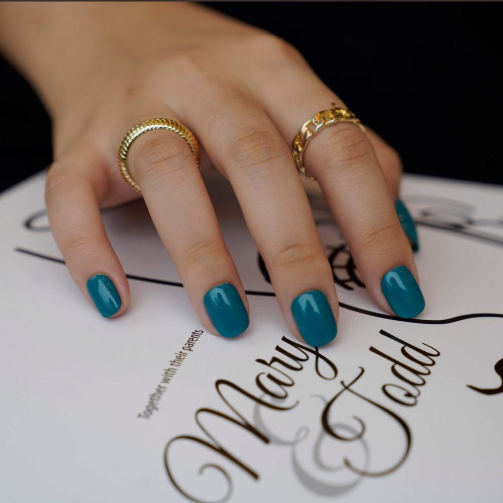 A set of teal glossy press - on nails neatly placed in a transparent box, showcasing a cool, smooth finish, ideal for beach or summer events.