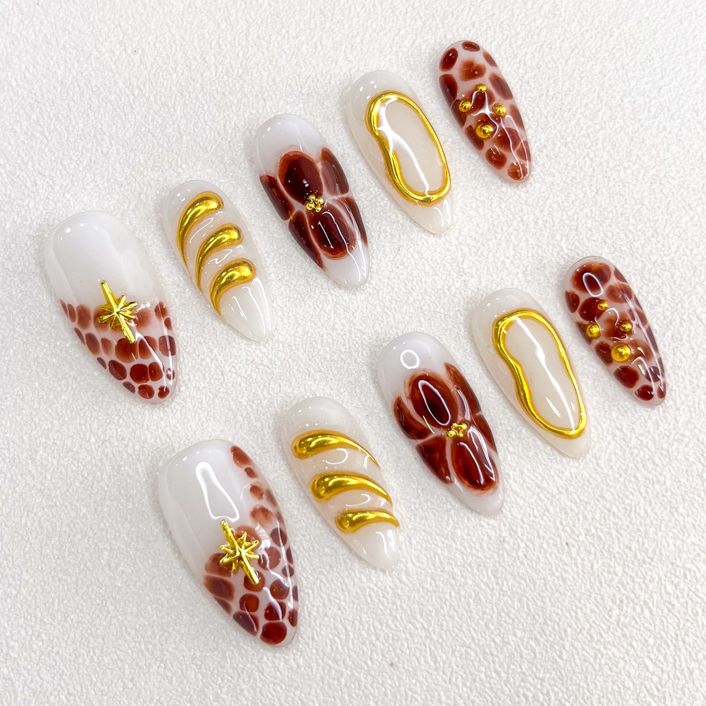 This is a press-on nail set featuring brown and gold tones with intricate marble patterns, floral motifs, and glossy textures. Designed for a stylish and luxurious appearance.