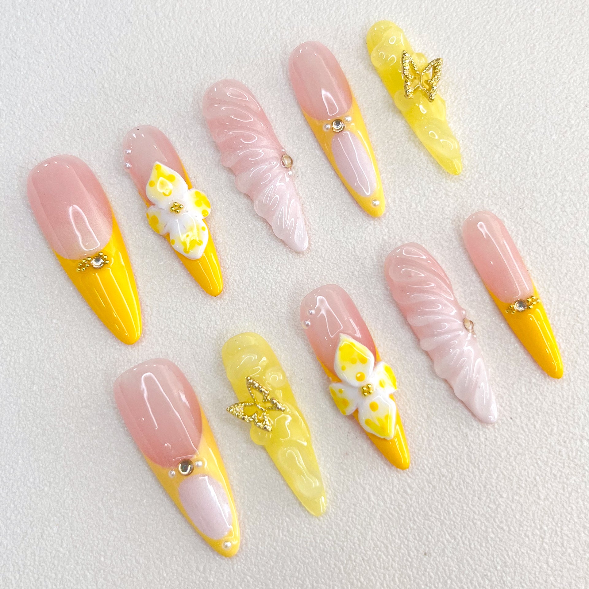 Sunshine Elegance press-on nails with yellow and pink hues, decorated with intricate butterfly and floral designs, adding a bright and feminine charm to any outfit.