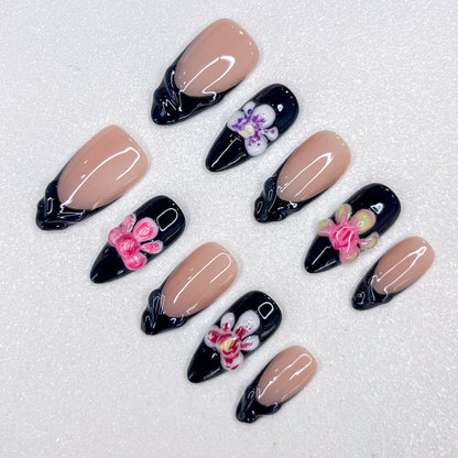 Midnight Orchid press-on nails with contrasting nude and black bases, highlighted by vibrant orchid details and glossy finishes for a modern, chic look.