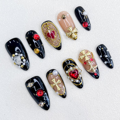 A set of bold and luxurious press-on nails featuring black and nude base tones, embellished with gold cross designs, red heart and round gemstones, pearls, and intricate metallic accents. The design exudes gothic elegance and a regal aesthetic.