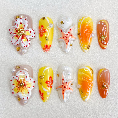 A colorful set of press-on nails with yellow, orange, and nude gradients, adorned with hand-painted flowers, starfish motifs, pearls, and gold foil accents. The design is vibrant and tropical, perfect for summer or beach-themed occasions.