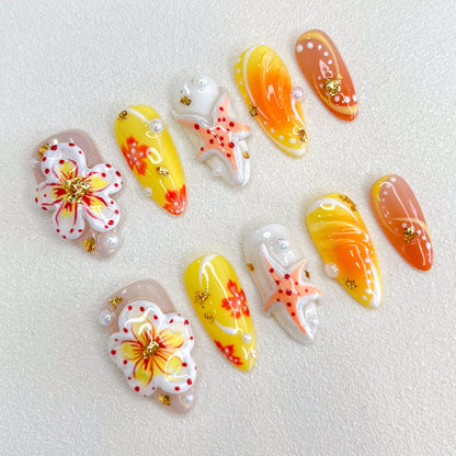 A colorful set of press-on nails with yellow, orange, and nude gradients, adorned with hand-painted flowers, starfish motifs, pearls, and gold foil accents. The design is vibrant and tropical, perfect for summer or beach-themed occasions.