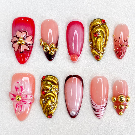 A glamorous set of press-on nails with red, pink, and nude tones, featuring 3D floral embellishments, gold accents, gradient effects, and intricate details. The design is romantic and elegant, perfect for special events or celebrations.