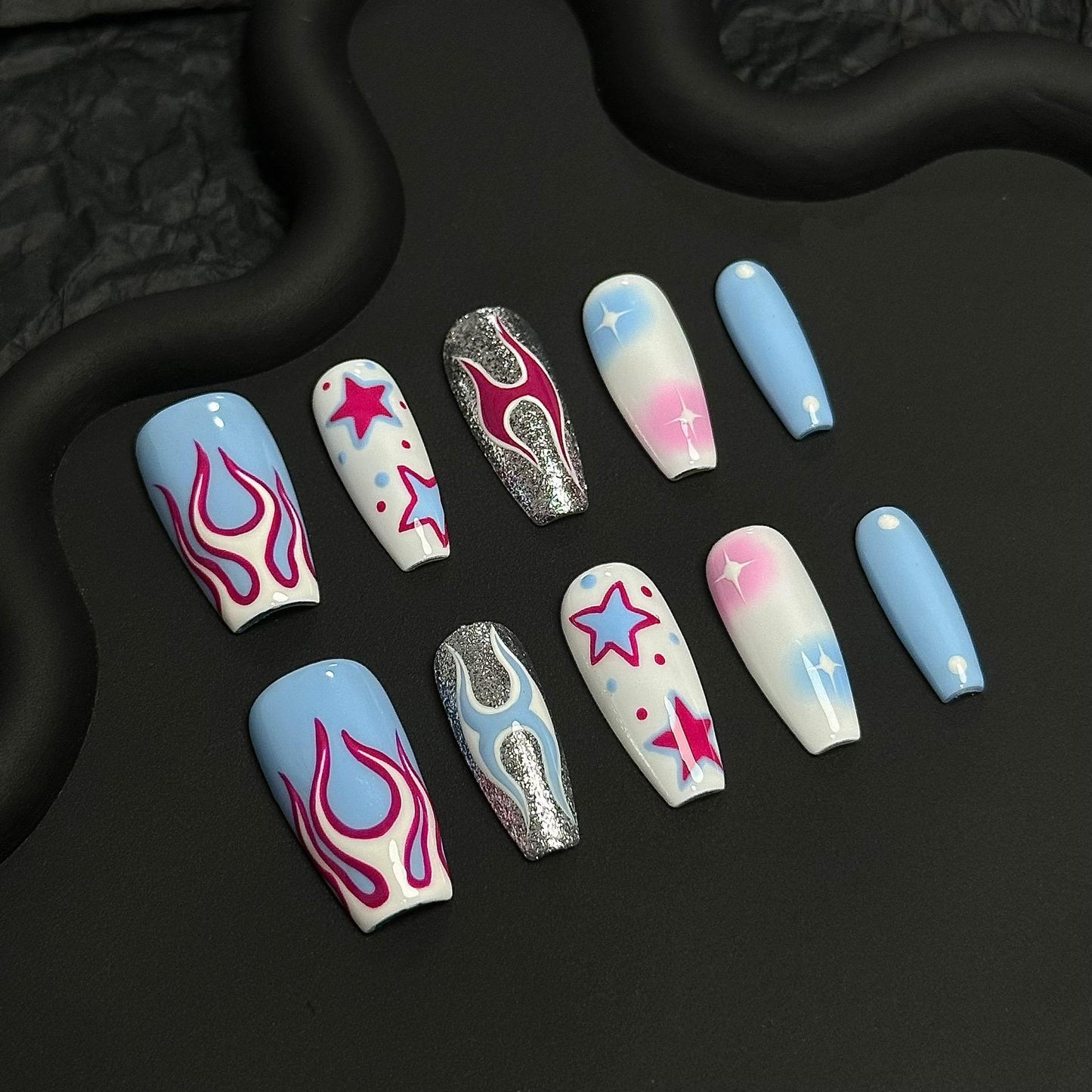 A press-on nail set featuring pink flames, starry designs, and pastel gradients with shimmering silver accents, creating a vibrant and edgy cosmic aesthetic.