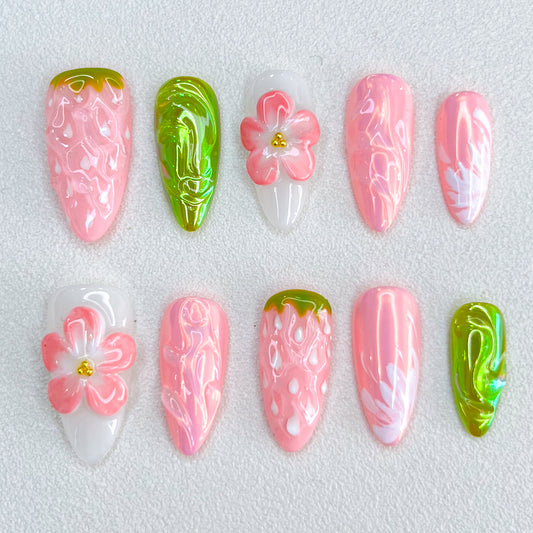 A strawberry-themed press-on nail set with textured berry details, delicate 3D flowers, and glossy green leaf-like accents. The pink and white hues blend beautifully, evoking a sweet and nature-inspired aesthetic.