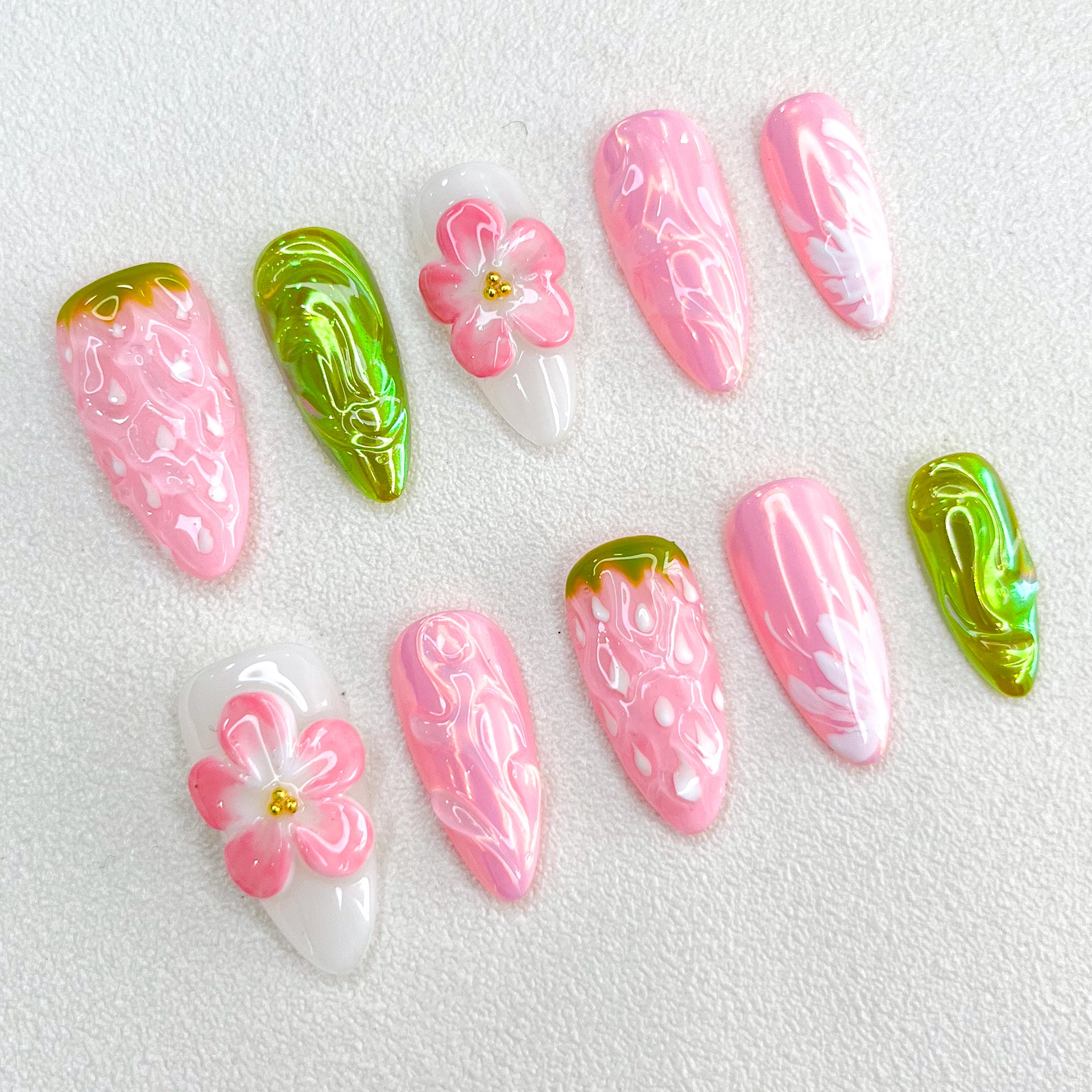 A strawberry-themed press-on nail set with textured berry details, delicate 3D flowers, and glossy green leaf-like accents. The pink and white hues blend beautifully, evoking a sweet and nature-inspired aesthetic.