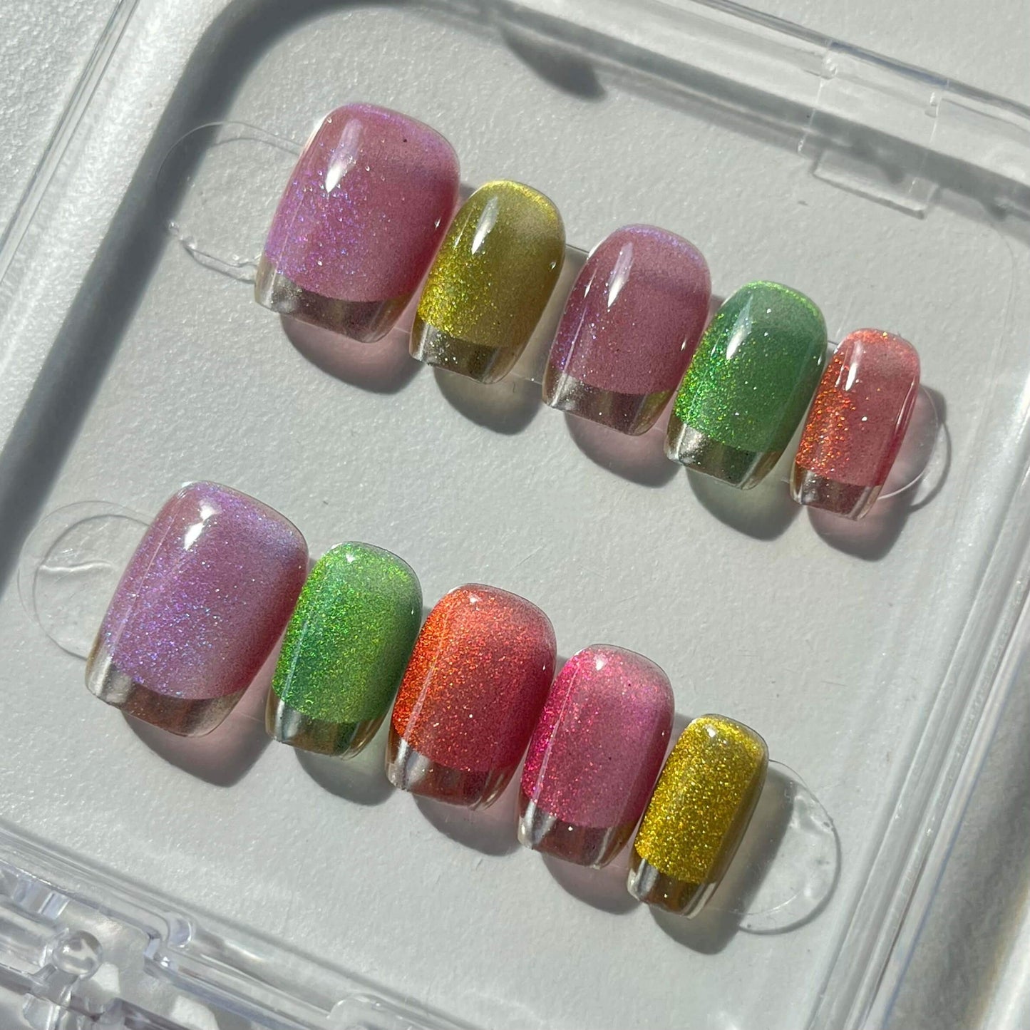 A set of multicolored glittery press - on nails neatly arranged in a transparent case. The nails feature a variety of bright colors with a sparkling finish, ideal for adding a festive and cheerful touch to your look, perfect for parties or celebratory events.