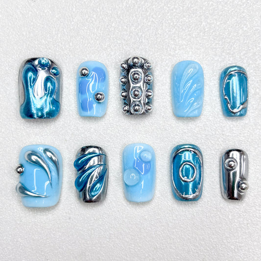 A cyber-inspired press-on nail set in icy blue and metallic chrome tones, featuring 3D orbs, abstract swirls, and smooth reflective patterns. A sleek, sci-fi style manicure with avant-garde vibes.