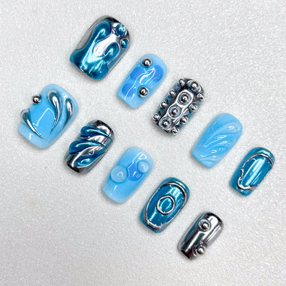 A cyber-inspired press-on nail set in icy blue and metallic chrome tones, featuring 3D orbs, abstract swirls, and smooth reflective patterns. A sleek, sci-fi style manicure with avant-garde vibes.