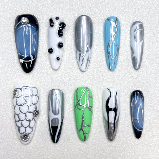 Press-on nails inspired by cyberpunk aesthetics, showcasing metallic silver veins across glossy black, green, blue, and white bases, accented with chrome details and geometric patterns for a bold techwear vibe.