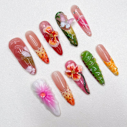 Colorful press-on nail set with tropical themes, showcasing 3D hibiscus flowers, butterflies, and floral gradients in pink, green, orange, and red, capturing a lush garden vibe.