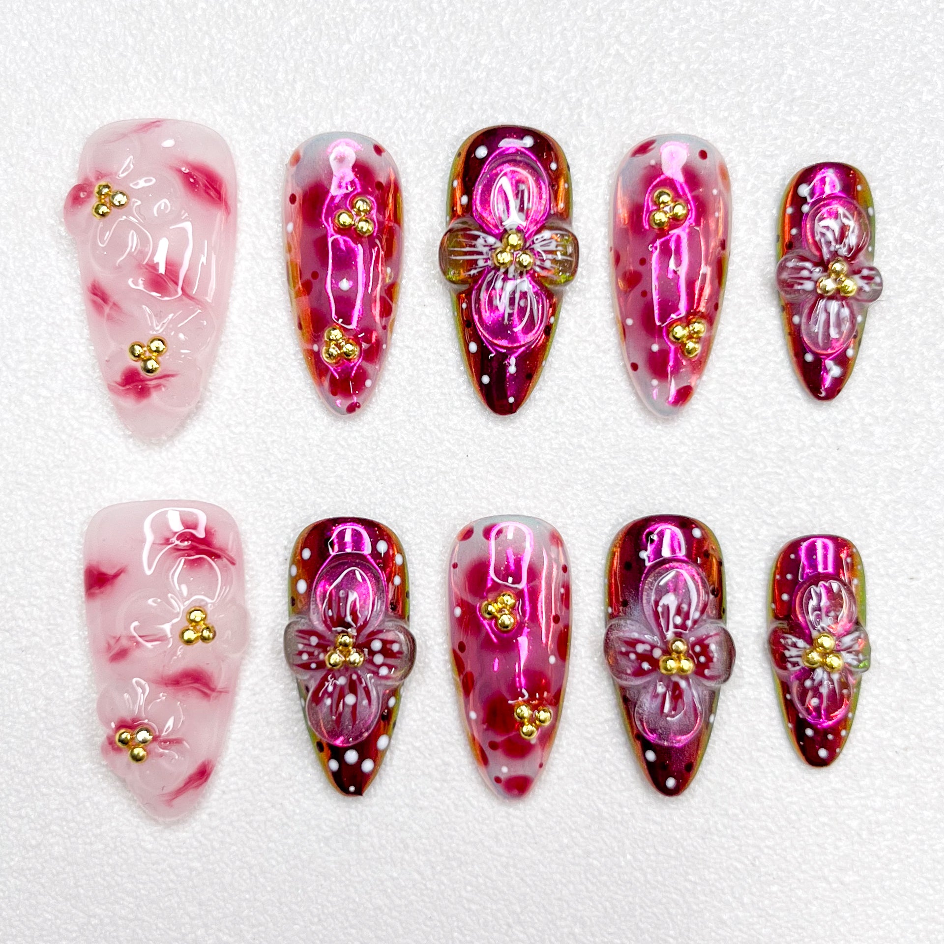 Glossy red and pink press-on nails with 3D flower details, golden bead centers, and shimmering gradient effects—elegant and bold for standout occasions.