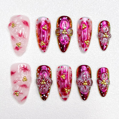 Glossy red and pink press-on nails with 3D flower details, golden bead centers, and shimmering gradient effects—elegant and bold for standout occasions.