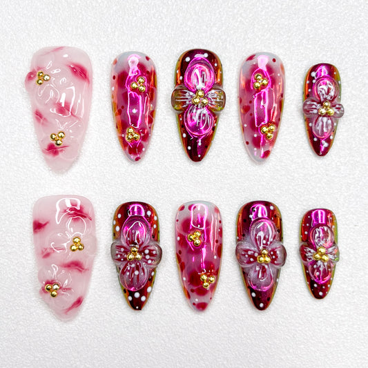 Glossy red and pink press-on nails with 3D flower details, golden bead centers, and shimmering gradient effects—elegant and bold for standout occasions.