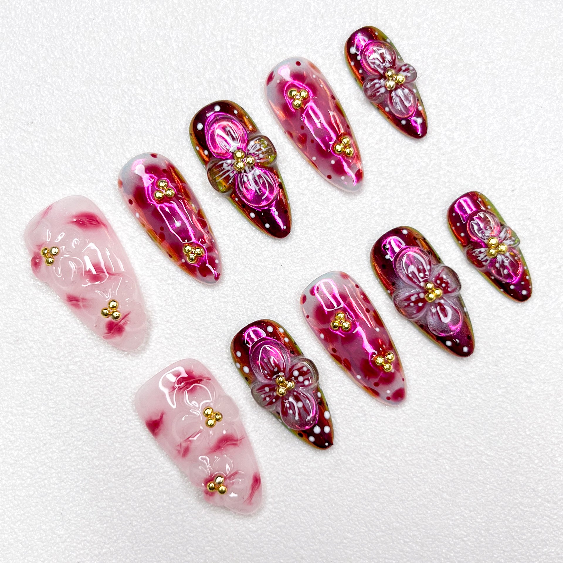Glossy red and pink press-on nails with 3D flower details, golden bead centers, and shimmering gradient effects—elegant and bold for standout occasions.