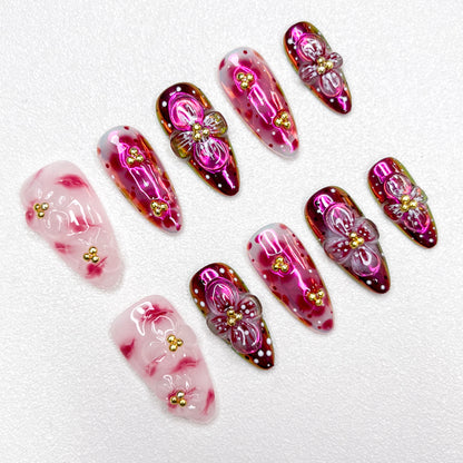 Glossy red and pink press-on nails with 3D flower details, golden bead centers, and shimmering gradient effects—elegant and bold for standout occasions.