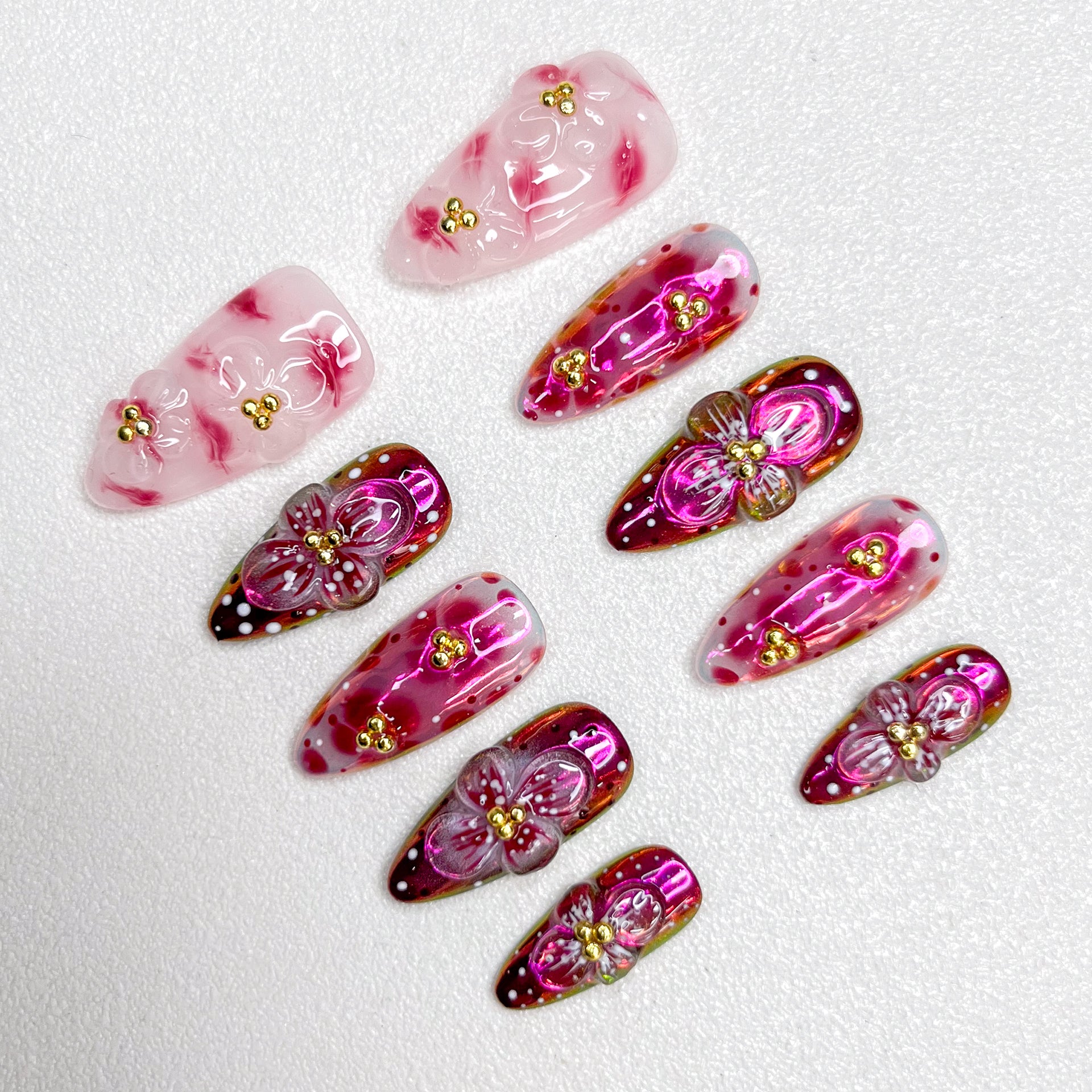 Glossy red and pink press-on nails with 3D flower details, golden bead centers, and shimmering gradient effects—elegant and bold for standout occasions.
