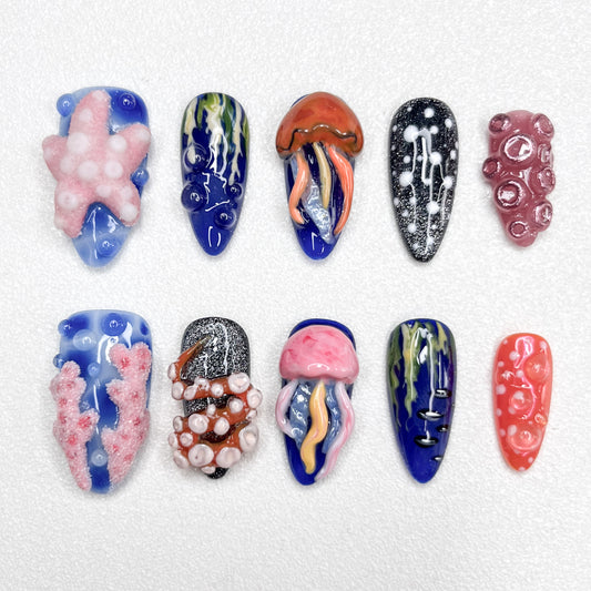 Hand-painted ocean-themed press-on nails with jellyfish, starfish, coral reef, and tentacle designs in deep blue, pink, and black tones—perfect for marine-inspired nail lovers.