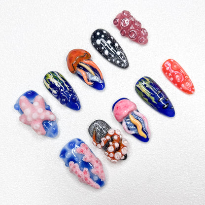 Hand-painted ocean-themed press-on nails with jellyfish, starfish, coral reef, and tentacle designs in deep blue, pink, and black tones—perfect for marine-inspired nail lovers.