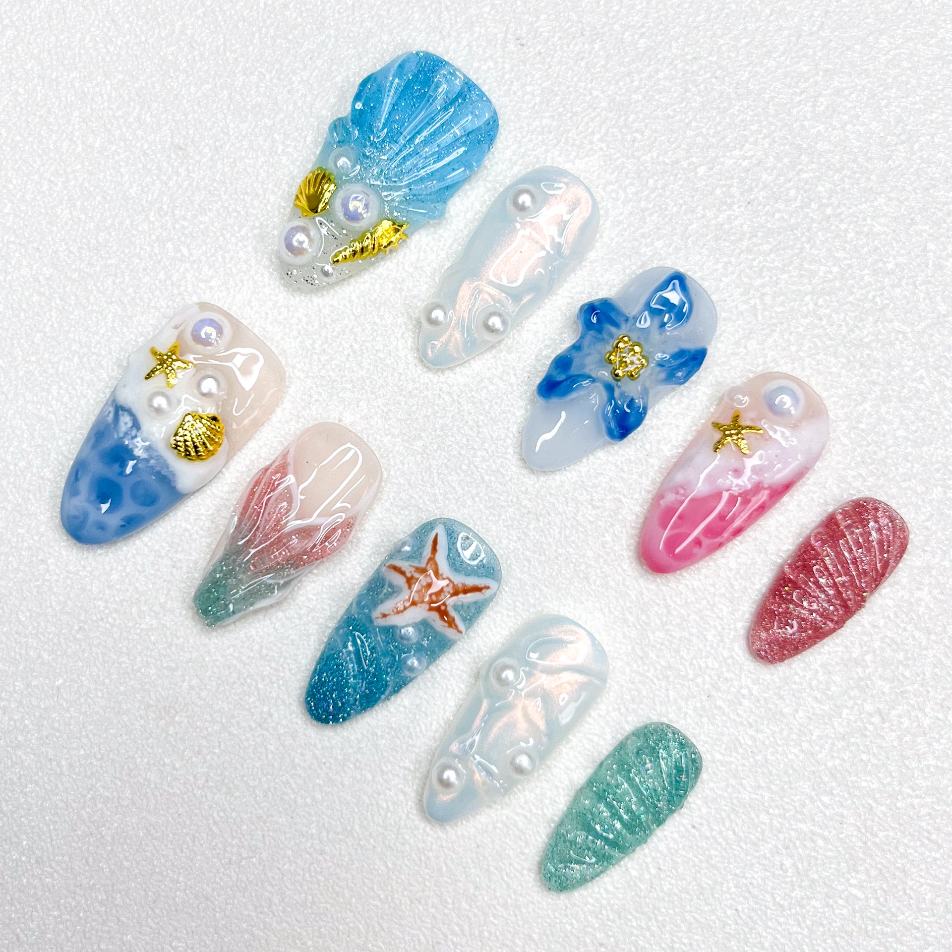 Mermaid-inspired press-on nails with blue and pink gradients, seashell textures, 3D pearls, gold seashell charms, and oceanic elements for dreamy undersea aesthetics.