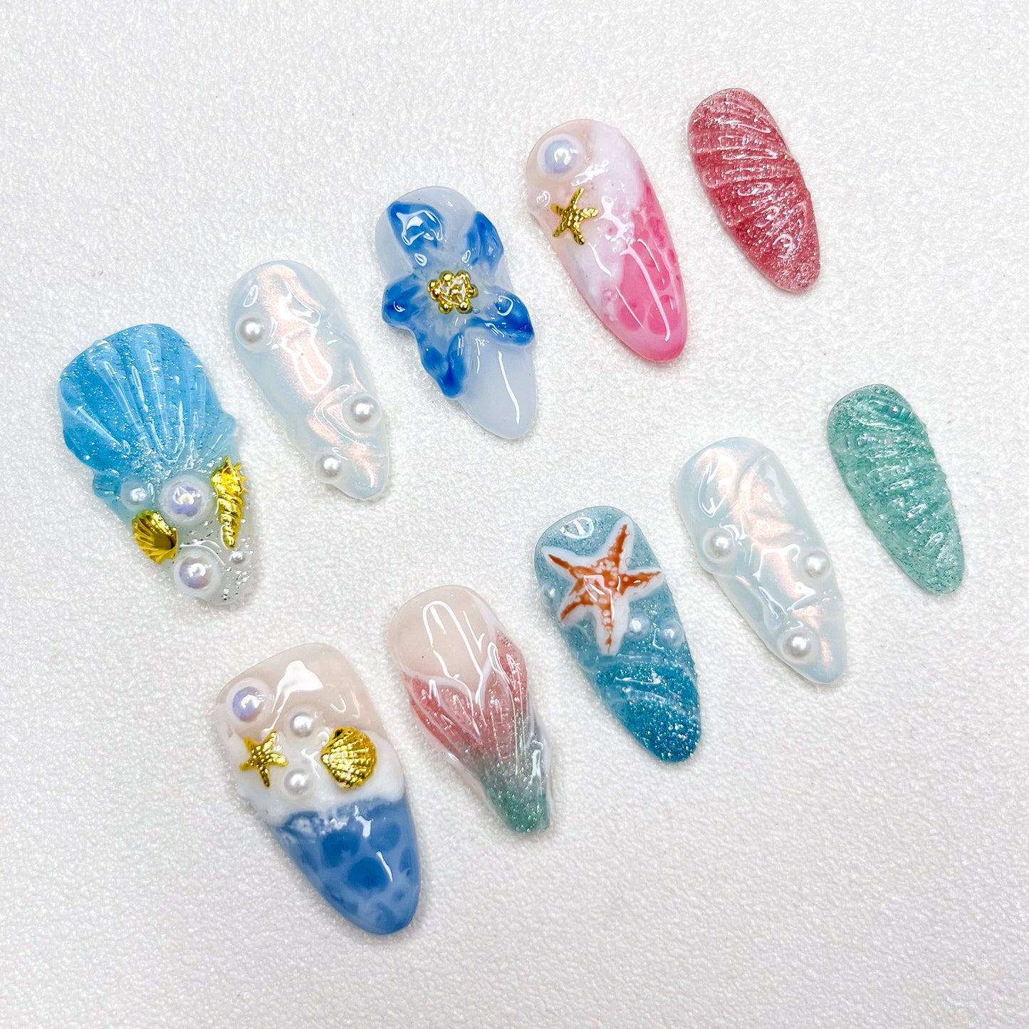 Mermaid-inspired press-on nails with blue and pink gradients, seashell textures, 3D pearls, gold seashell charms, and oceanic elements for dreamy undersea aesthetics.