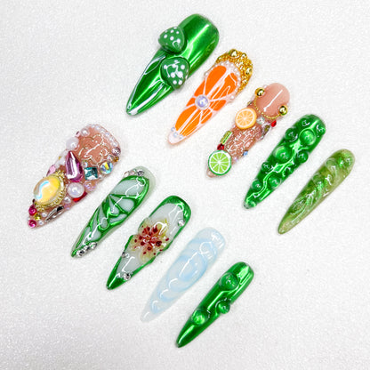A vibrant nature-inspired press-on nail set with glossy green finishes, mushrooms, citrus fruits, flower petals, and gemstone embellishments, resembling a fantasy garden or enchanted forest.