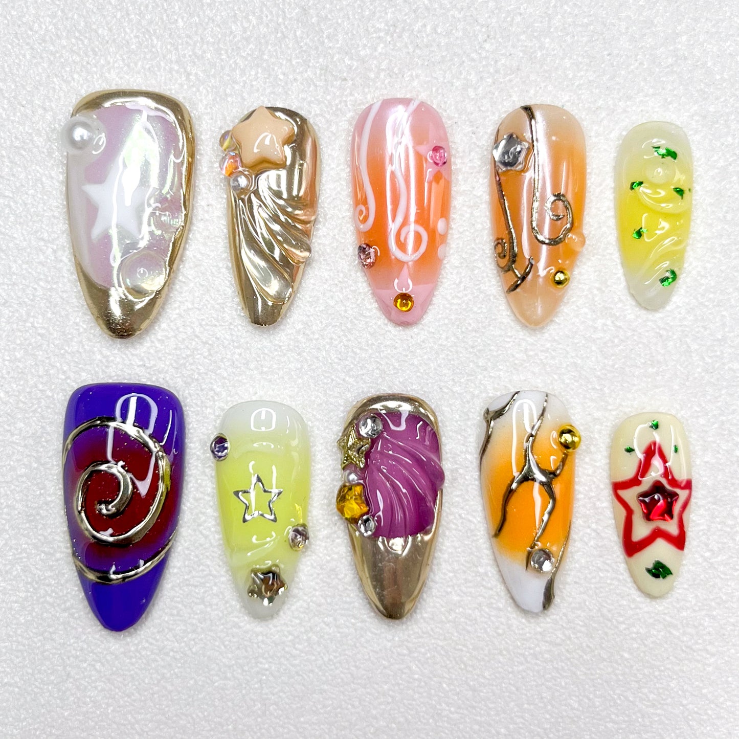 Galaxy-inspired press-on nails with star motifs, music notes, swirl designs, and metallic accents. Features shades of purple, gold, yellow, and orange, blended with celestial themes and 3D embellishments.