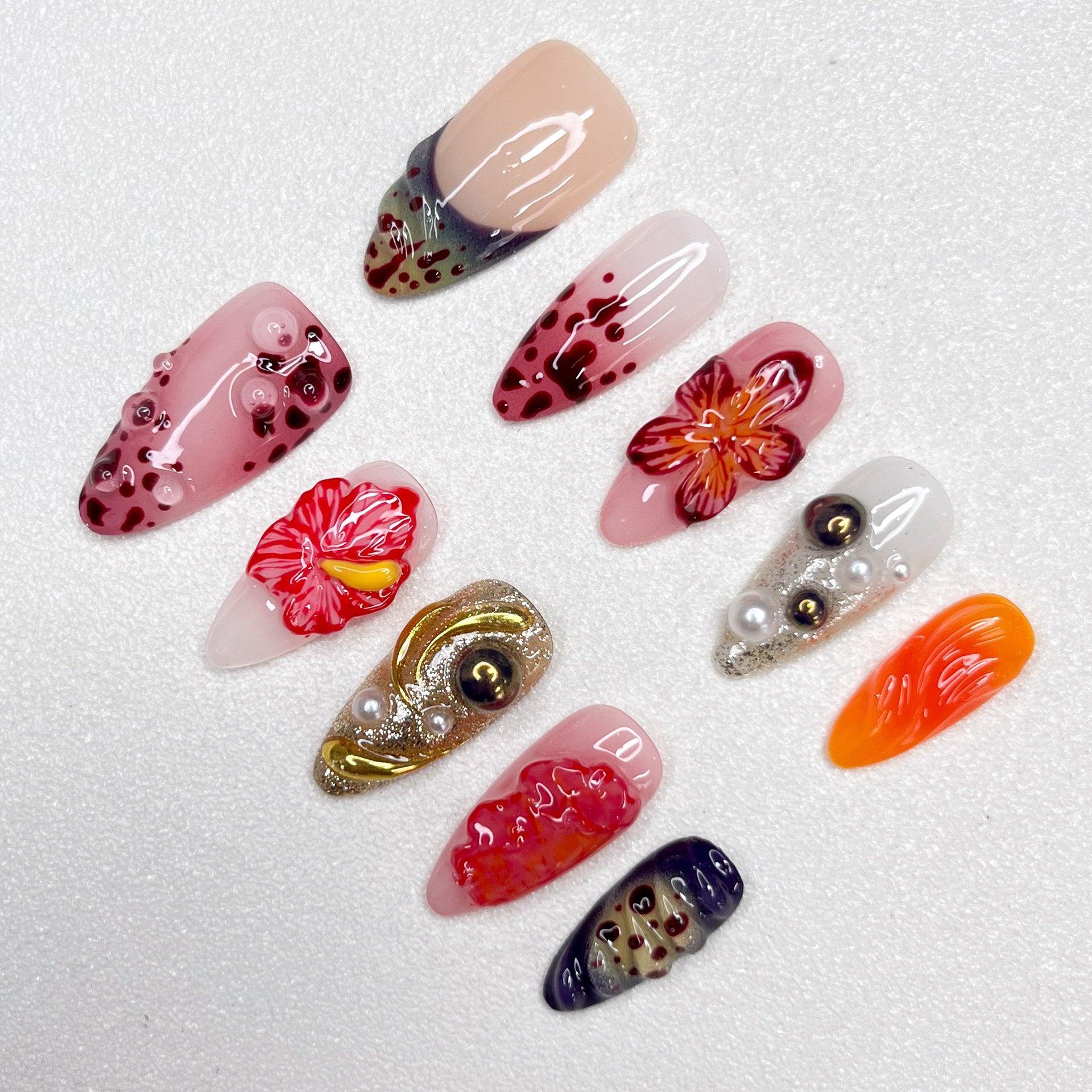 Press-on nails with lava-inspired gradients, red hibiscus flowers, metallic gold swirls, and bubble textures. Includes pearl embellishments and fire-orange, deep wine, and ash grey accents, evoking volcanic eruption and floral bloom.