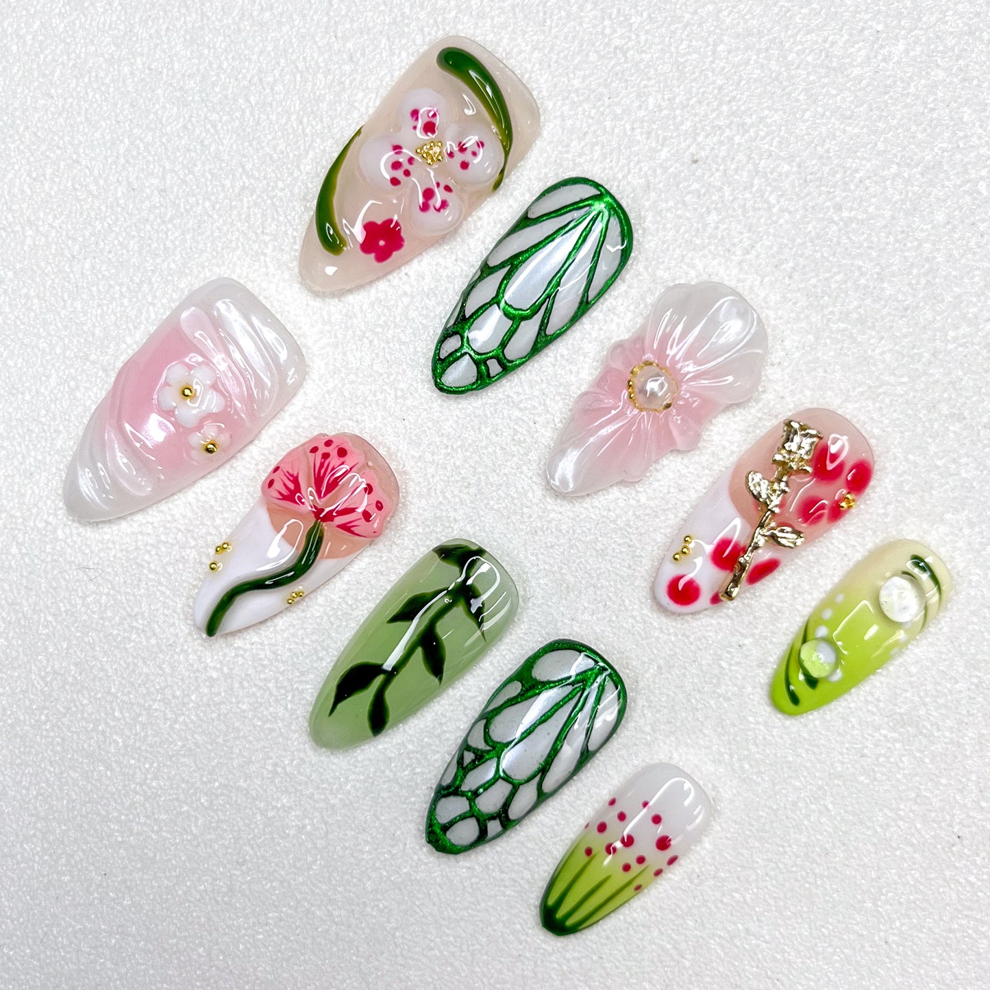 Nature-inspired press-on nails with translucent flowers, gold floral charms, vein-like green outlines, soft pink and white petals, and hand-painted leaves. The design blends garden florals with minimalist elegance in spring tones.