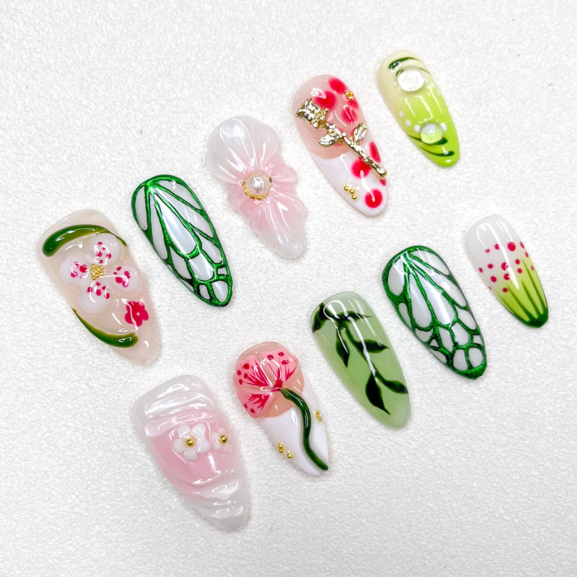 Nature-inspired press-on nails with translucent flowers, gold floral charms, vein-like green outlines, soft pink and white petals, and hand-painted leaves. The design blends garden florals with minimalist elegance in spring tones.