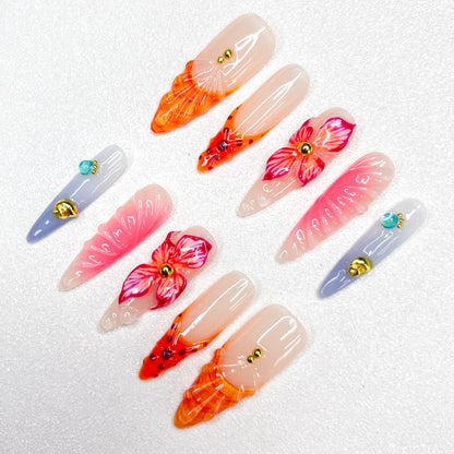 Press-on nails with fiery orange and pink flame tips, vivid hibiscus flower accents, soft gradient backgrounds, and gold studs. Featuring 3D floral textures and translucent jelly finishes, evoking tropical sunsets and vibrant blooms.