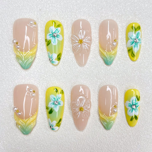 Press-on nails with a lemon-yellow and mint-green gradient design, decorated with 3D translucent flowers, hand-painted teal-blue blossoms, pearl accents, and nude-toned bases. A bright botanical-inspired summer nail set.