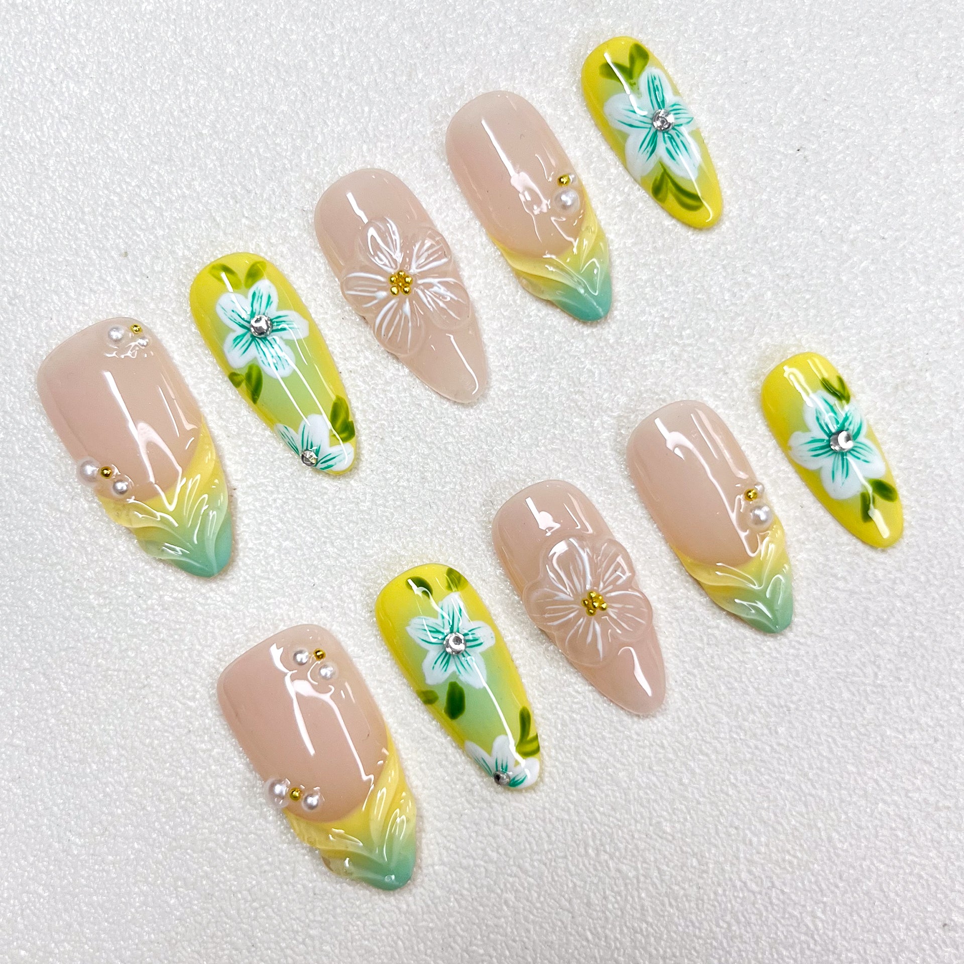 Press-on nails with a lemon-yellow and mint-green gradient design, decorated with 3D translucent flowers, hand-painted teal-blue blossoms, pearl accents, and nude-toned bases. A bright botanical-inspired summer nail set.