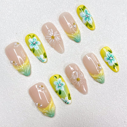 Press-on nails with a lemon-yellow and mint-green gradient design, decorated with 3D translucent flowers, hand-painted teal-blue blossoms, pearl accents, and nude-toned bases. A bright botanical-inspired summer nail set.