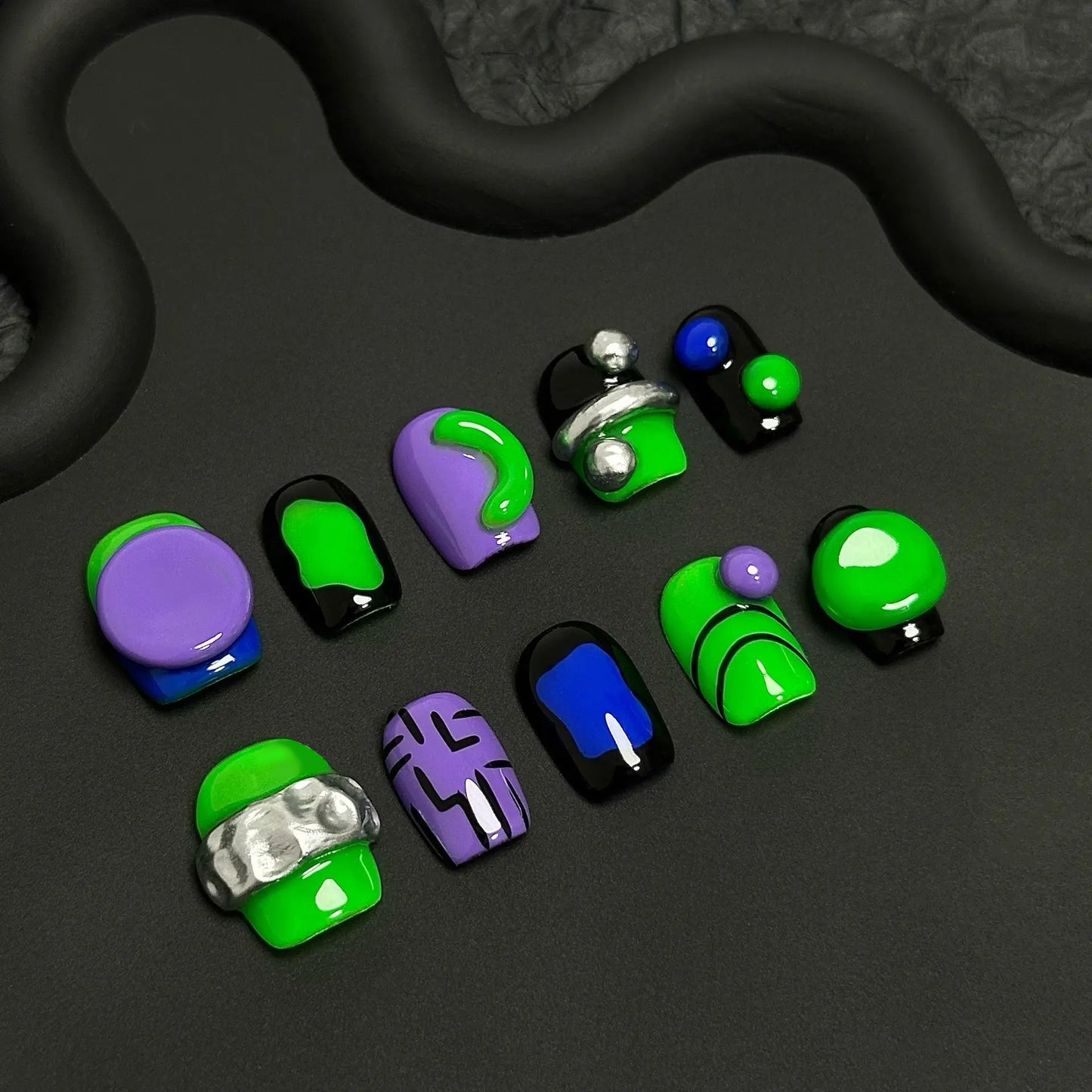 A press-on nail set featuring vibrant green and purple designs with black accents, metallic silver details, and 3D elements, creating a futuristic and modern aesthetic.