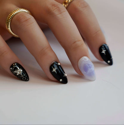 A cosmic-themed press-on nail set with a combination of black and pastel blue nails. The black nails feature glittery silver stars and rhinestones, while the blue nails include elegant bow designs. Perfect for a celestial and dreamy style.