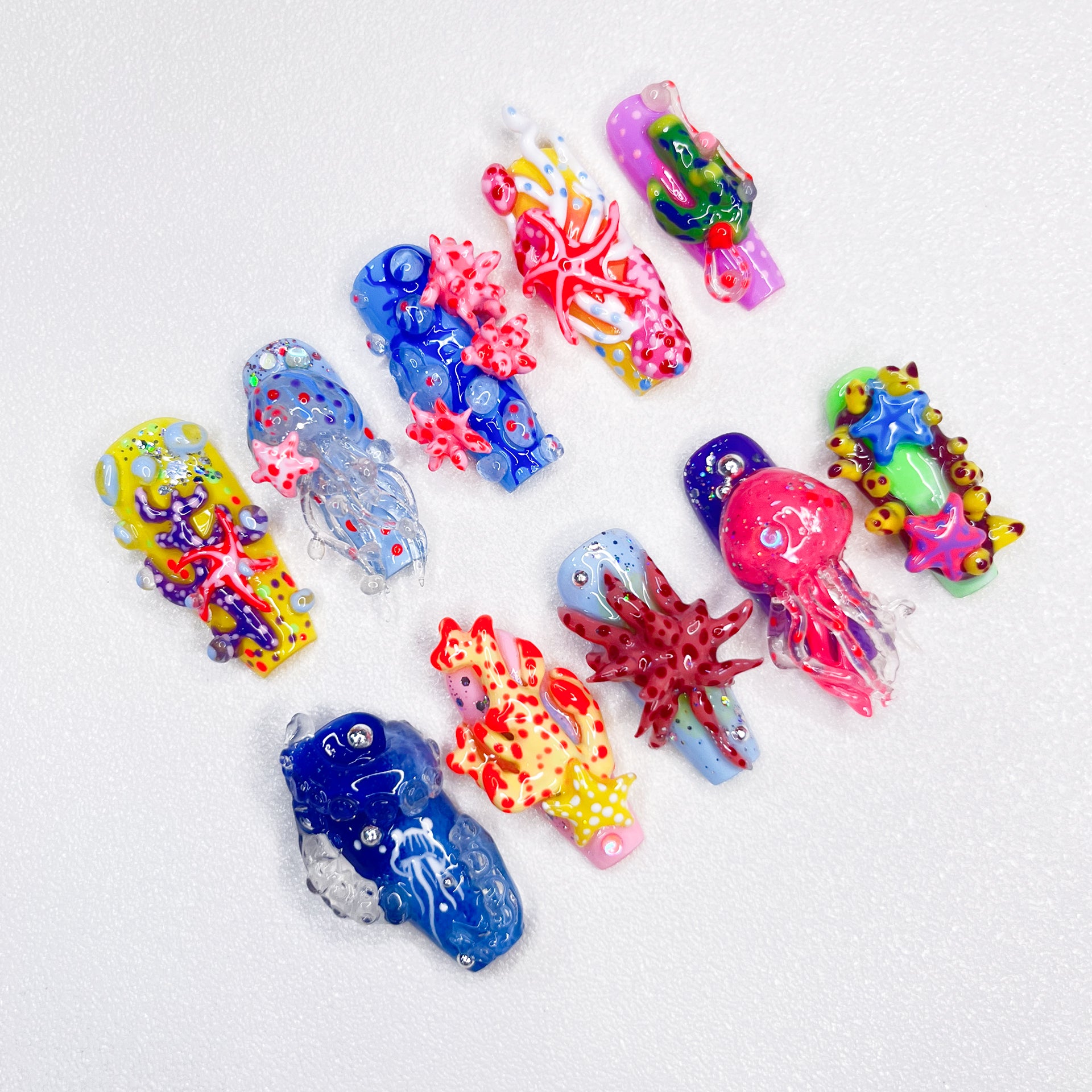 A set of ocean-themed press-on nails showcasing intricate 3D details of coral reefs, starfish, jellyfish, and vibrant underwater designs in blue, yellow, red, and green tones.