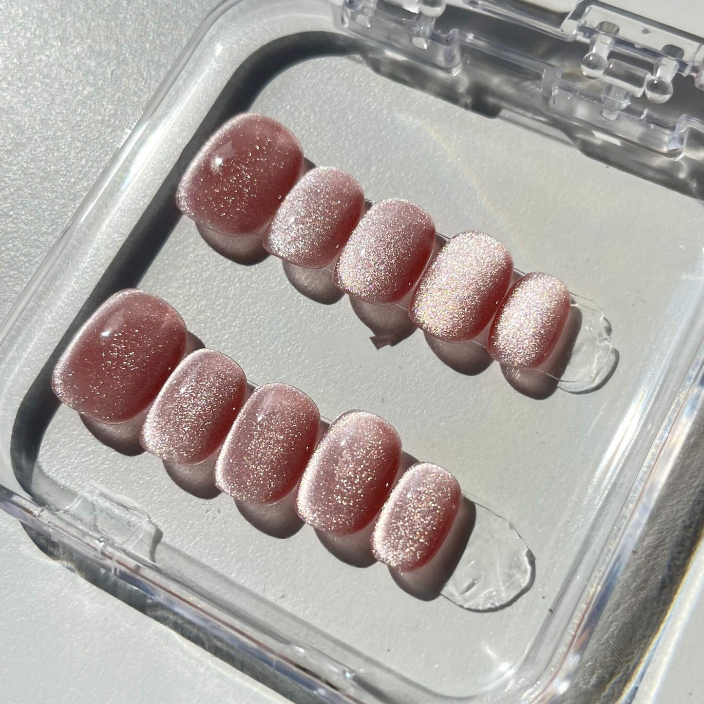 A set of rose - colored press - on nails with a subtle shimmer, neatly arranged in a transparent case. The nails have a soft, glowing finish, ideal for creating a romantic and elegant look, suitable for dates or special occasions.