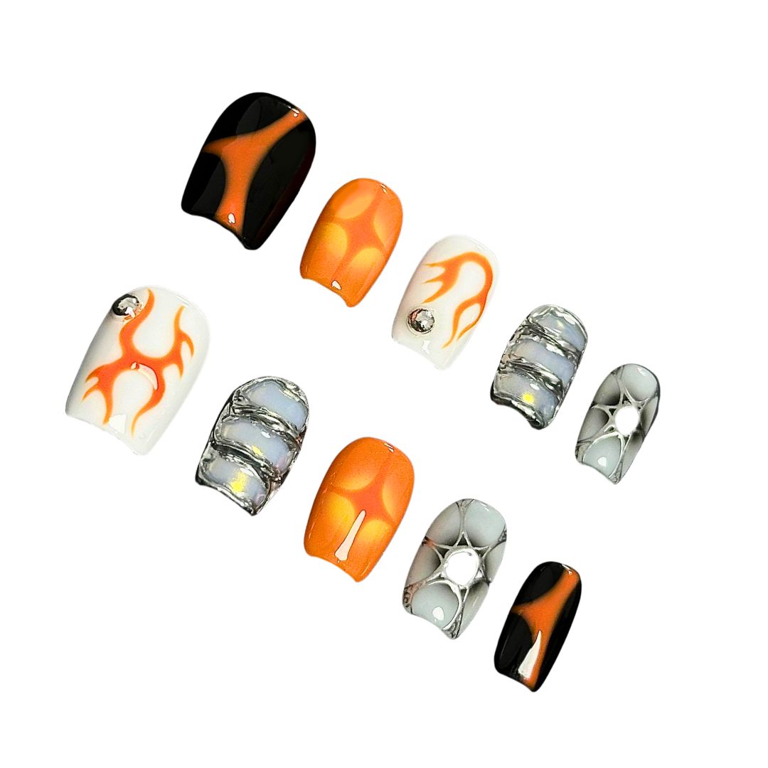 A press-on nail set with orange flame designs, glossy black and white bases, and metallic silver accents, creating a bold and futuristic aesthetic.