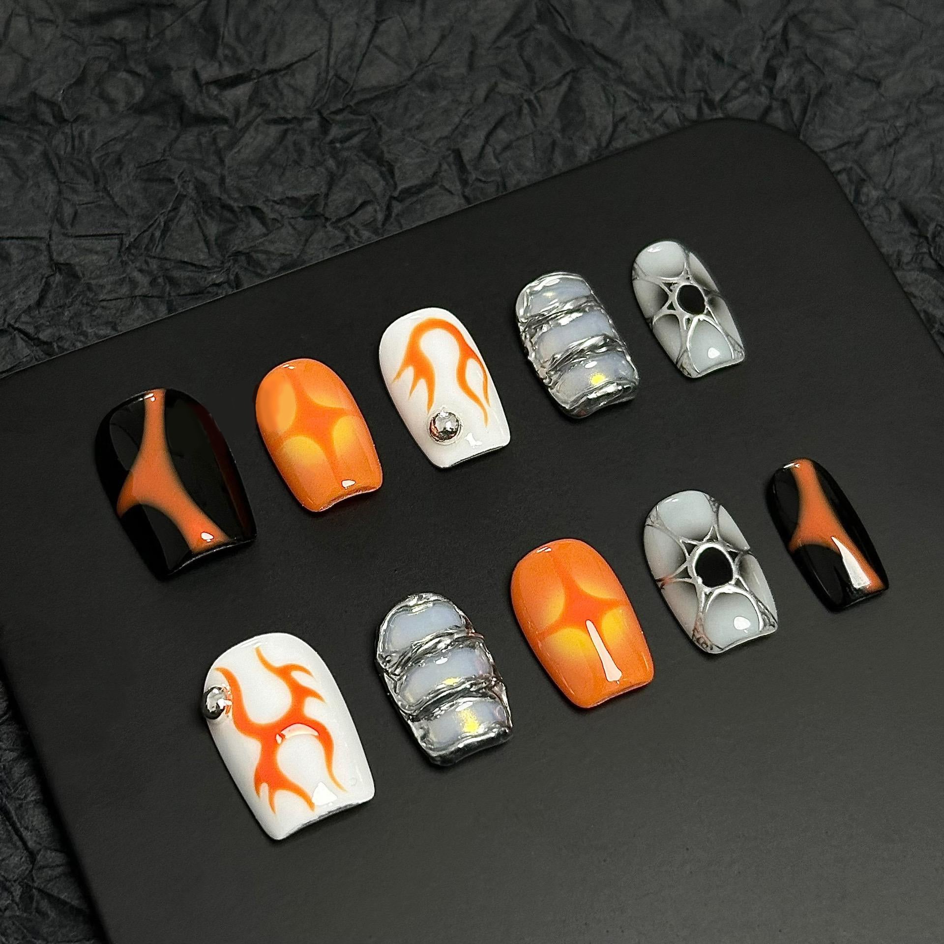 A press-on nail set with orange flame designs, glossy black and white bases, and metallic silver accents, creating a bold and futuristic aesthetic.