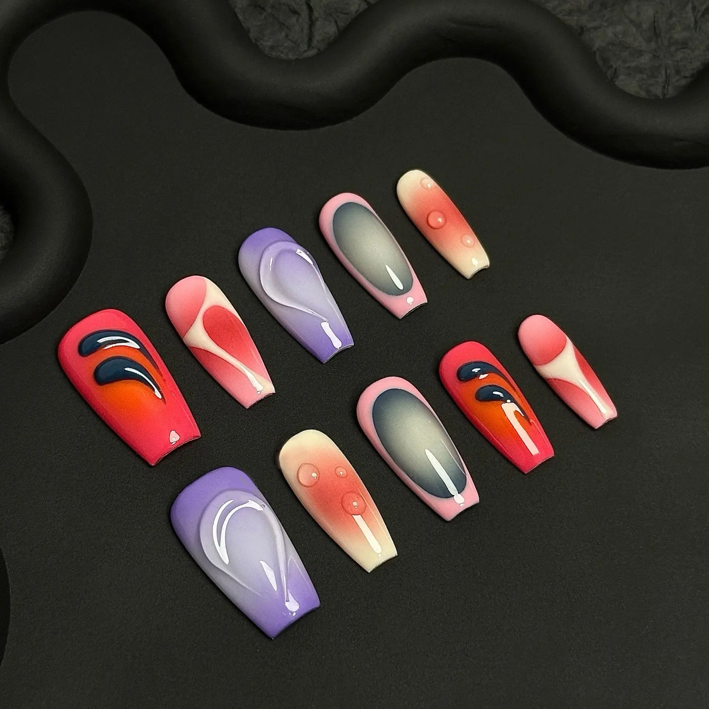 A press-on nail set featuring pink, purple, and red gradients with abstract glossy patterns and 3D droplet effects, creating a bold and artistic aesthetic.