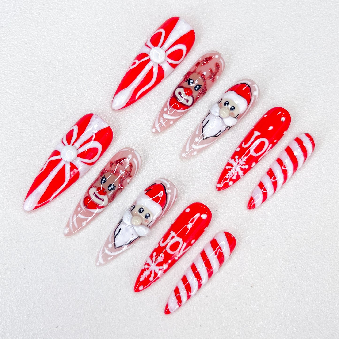 Christmas-themed press-on nails with Santa, reindeer, candy cane, gift box, and "JOY" text designs.