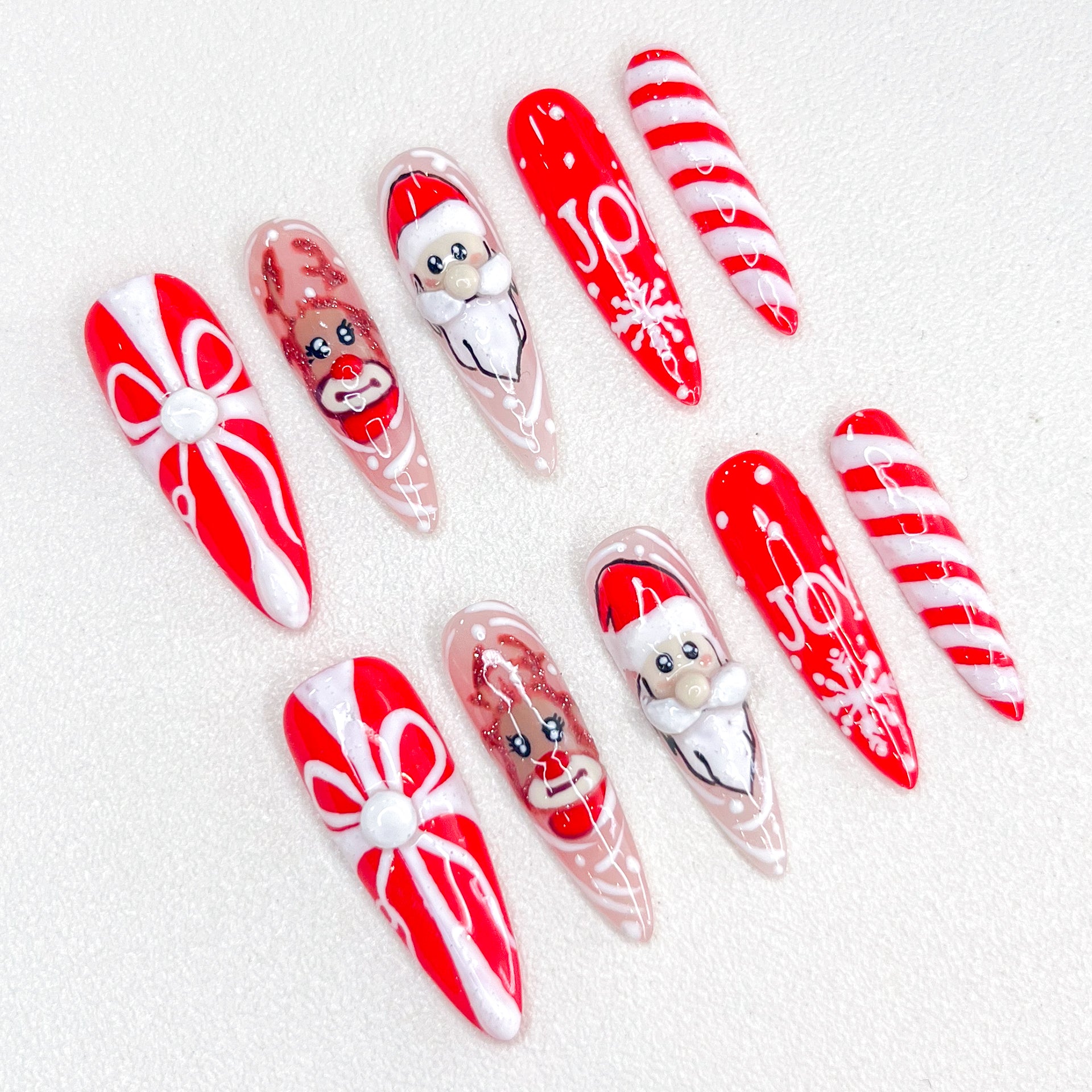 Christmas-themed press-on nails with Santa, reindeer, candy cane, gift box, and "JOY" text designs.